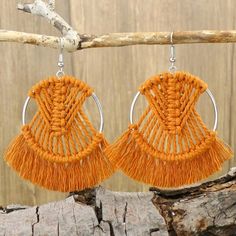 two pairs of orange tasseled earrings hanging from a tree branch with wood planks in the background