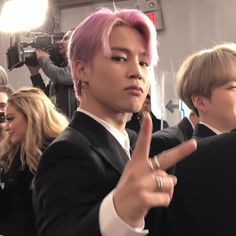 a man with pink hair giving the middle finger sign in front of people taking pictures