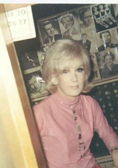 an old photo of a woman sitting in front of a wall with pictures on it