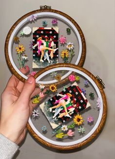 two embroidery hoop frames with pictures of people on them and flowers in the middle, one being held by a person's hand