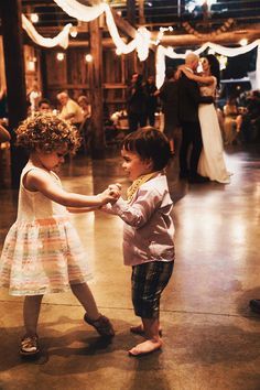 two young children are dancing together on the dance floor at a wedding reception in an old barn