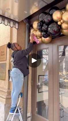 a woman standing on a stepladder in front of a building with lots of balloons