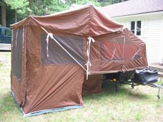 a tent is set up on the grass in front of a house with a trailer attached to it