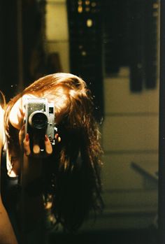 a woman holding up a camera to take a photo in front of a mirror with her hair blowing back