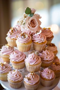 cupcakes with pink frosting and gold decorations on a cake platter in front of candles