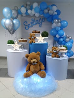 a teddy bear sitting on top of a cloud in front of blue and white balloons