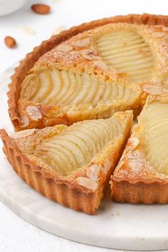 an apple tart on a white plate with almonds around the edges and one slice cut out