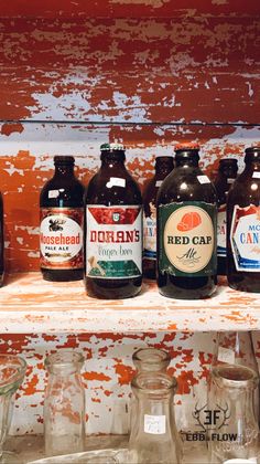 several different types of beer bottles on a shelf in front of an orange painted wall