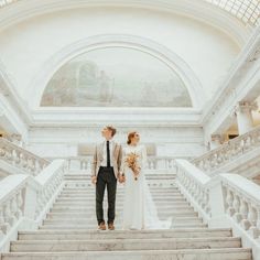 a bride and groom are standing on the stairs at their wedding ceremony in an ornate building