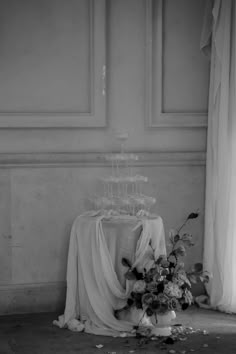 an arrangement of flowers sits on the floor next to a table with a cloth draped over it