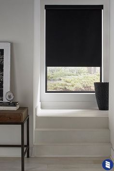 a window with black shades in a white room next to a table and planter