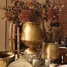 a table topped with gold vases filled with lots of flowers next to plates and cups