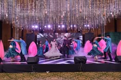 a group of people dancing on stage with chandeliers hanging from the ceiling behind them