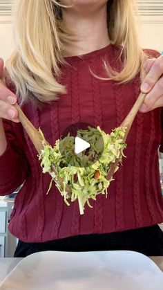 a woman holding a wooden spoon filled with lettuce