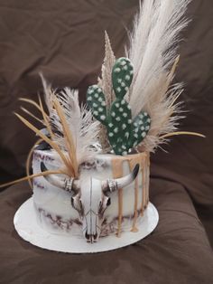 a cake decorated with an animal skull, cactus and feathers on a white platter