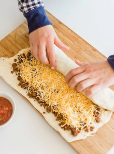 a person is making a pizza with cheese and sauce on the counter next to a wooden cutting board