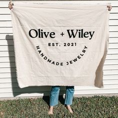 a woman holding up a white towel that says olive + wiley