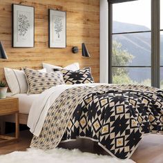 a bedroom with wooden walls and flooring has a black and white quilt on the bed