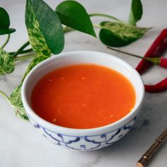 a bowl of tomato soup next to two chili peppers and a leafy green plant