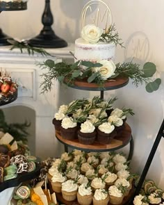 three tiered cake stand with cupcakes and flowers on each tier, decorated with greenery