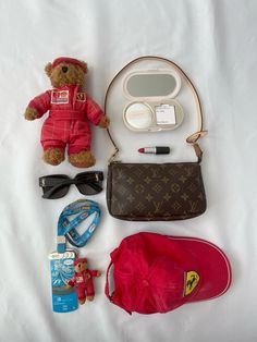 a teddy bear, sunglasses, hat, and other items laid out on a bed