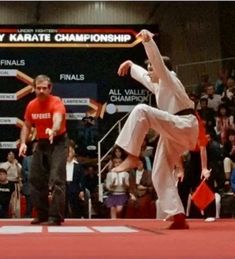 two men are doing karate moves in front of an audience at a competition, while one man is holding his leg up