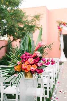 an arrangement of flowers and greenery is on the back of a white chair at a wedding ceremony