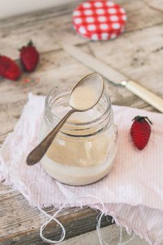 a spoon sitting on top of a glass jar filled with cream next to strawberries