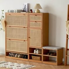 a wooden cabinet sitting next to a white wall with shoes on it and a rug