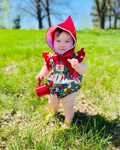 a baby girl wearing a red hoodie and floral bloomy romper in the grass