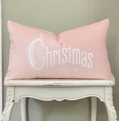 a pink christmas pillow sitting on top of a white table next to a mirror and chair