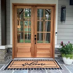 a welcome mat is on the front door of a house with two doors and flowers