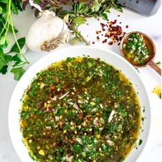 a white bowl filled with green soup next to garlic and herbs