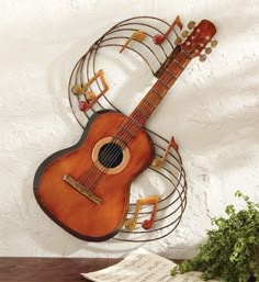 a wooden guitar hanging on the wall next to music notes and a potted plant