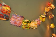 colorful paper decorations hanging from clothes pins on a wall with lights in the corner behind them