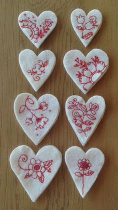 six embroidered hearts with flowers on them sitting on a wooden table next to each other