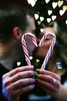 a man and woman kissing while holding candy canes