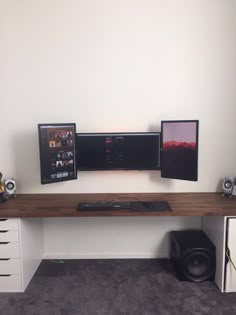 a desk with two monitors and speakers on it in front of a wall mounted speaker system