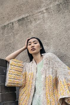 a woman leaning against a wall with her hand on her head and wearing a colorful shawl