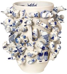 a white vase with blue and white designs on the bottom is surrounded by smaller ceramic objects