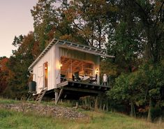 a small white house sitting on top of a lush green hillside next to trees and grass