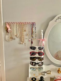 a white table topped with lots of jewelry and sunglasses next to a mirror on the wall