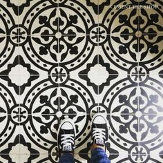 someone's feet standing on a black and white tile floor with an intricate pattern