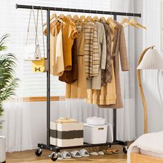 a rack with clothes hanging on it next to a bed and a plant in a room