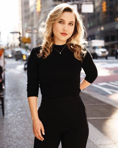 a woman standing on the side of a road wearing black pants and a black top