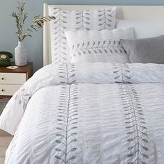 a bed with white and grey comforters in a bedroom next to a night stand