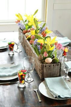 a wooden crate filled with flowers on top of a table next to plates and silverware