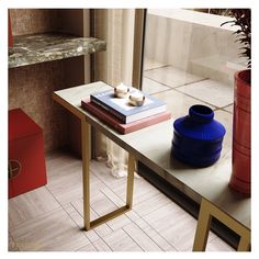 a table with two books on it next to a red vase and other items in front of a window