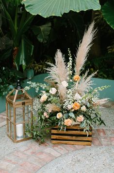 an arrangement of flowers and plants in a wooden box on a brick floor next to a lantern