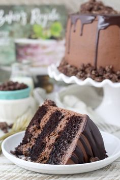 a slice of chocolate cake on a plate with the rest of the cake in the background